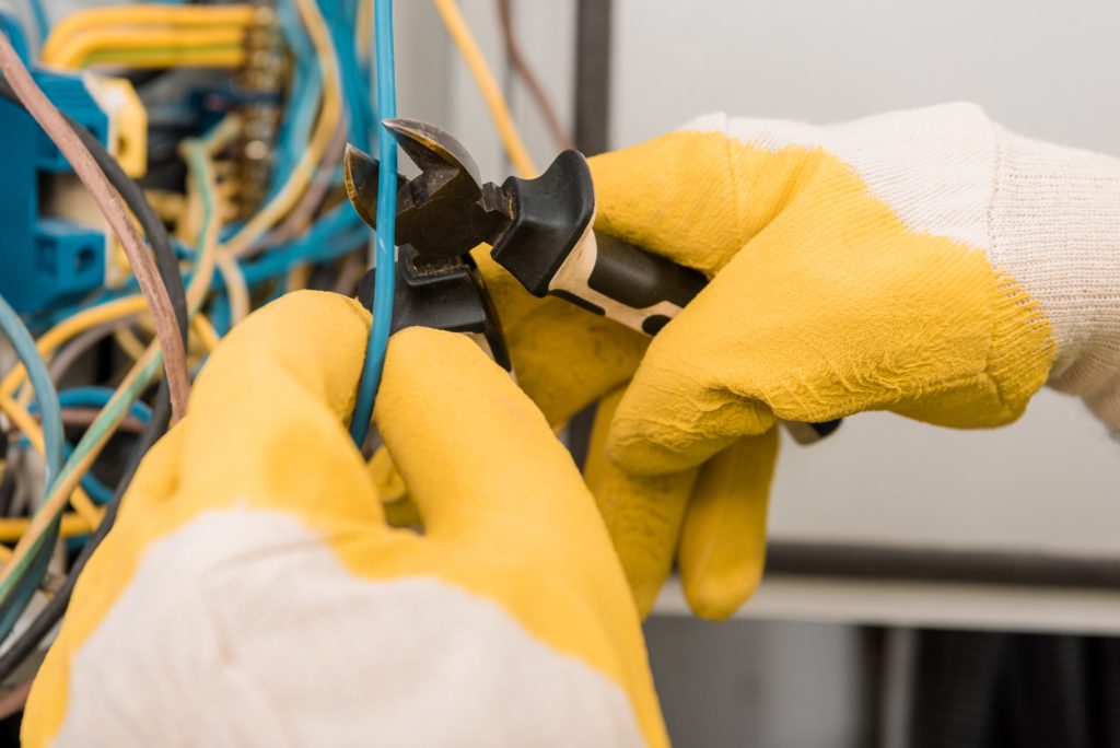 cropped image on electrician cutting wires from electrical panel with pliers in corridor